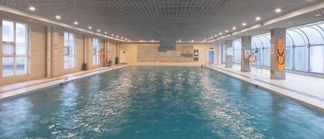 An indoor swimming pool with clear water, tiled walls, and a ceiling with a grid pattern.