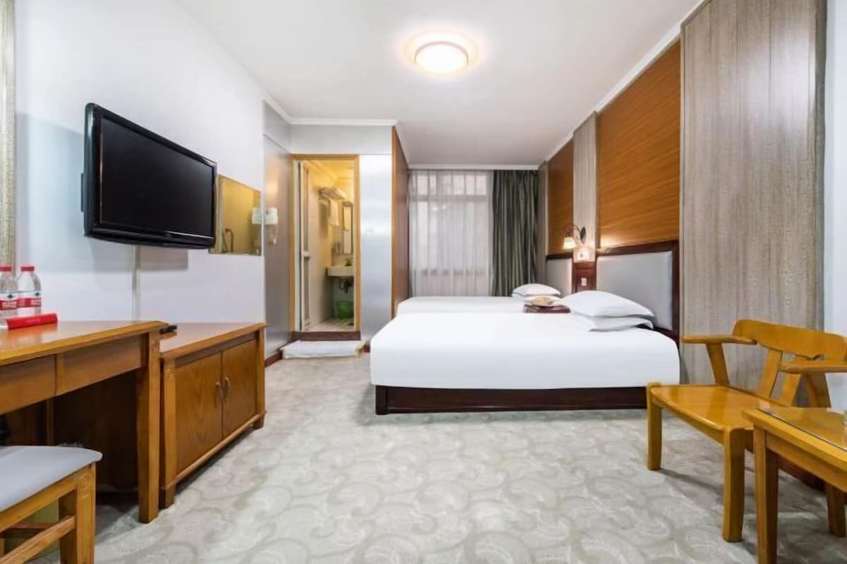 A hotel room with a bed, a desk, a chair, a television, and a bathroom visible through an open door.