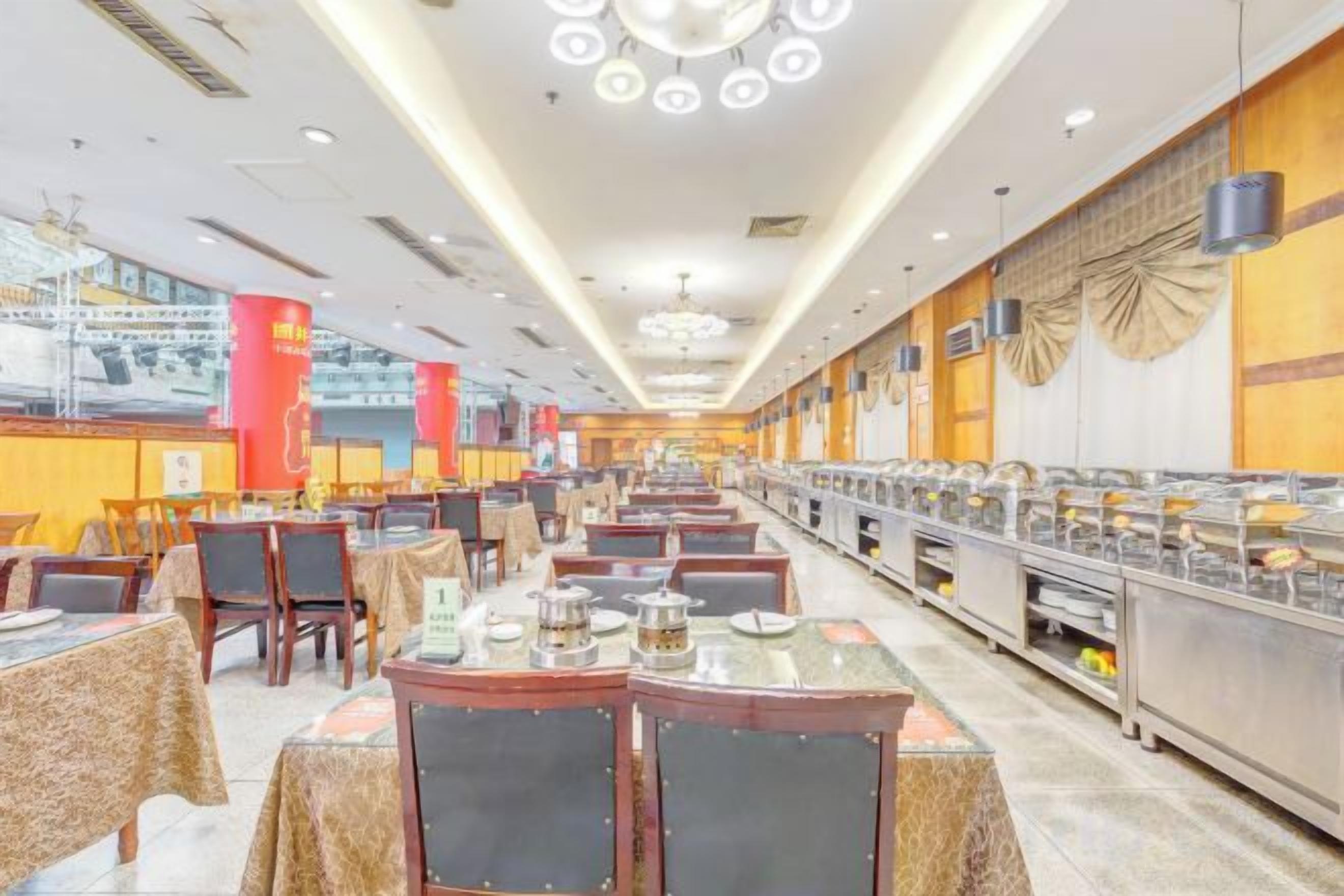 A spacious cafeteria with multiple tables and chairs, a buffet line, and a high ceiling with circular light fixtures.