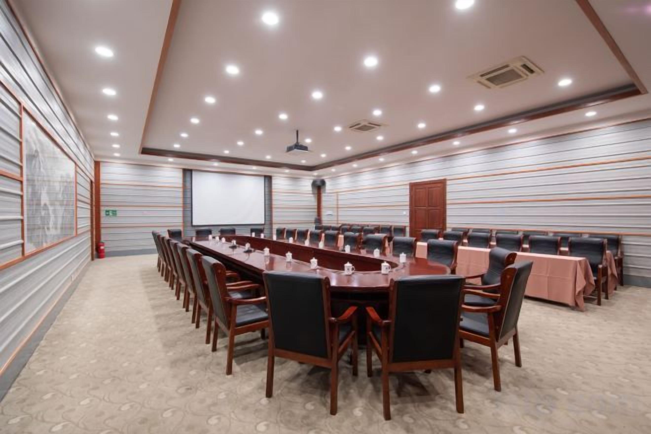 A conference room with a long table, chairs, and a projector screen.