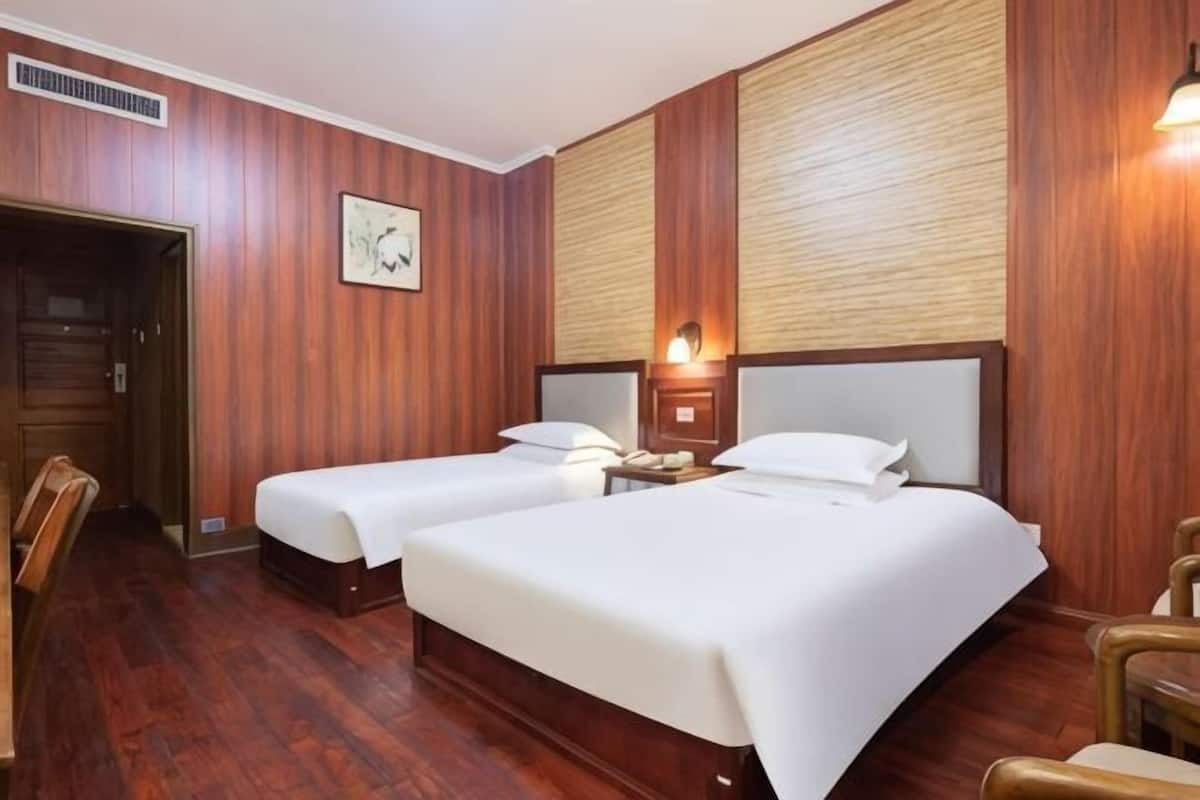 A hotel room with two beds, wooden walls, a door, a nightstand, and a chair.