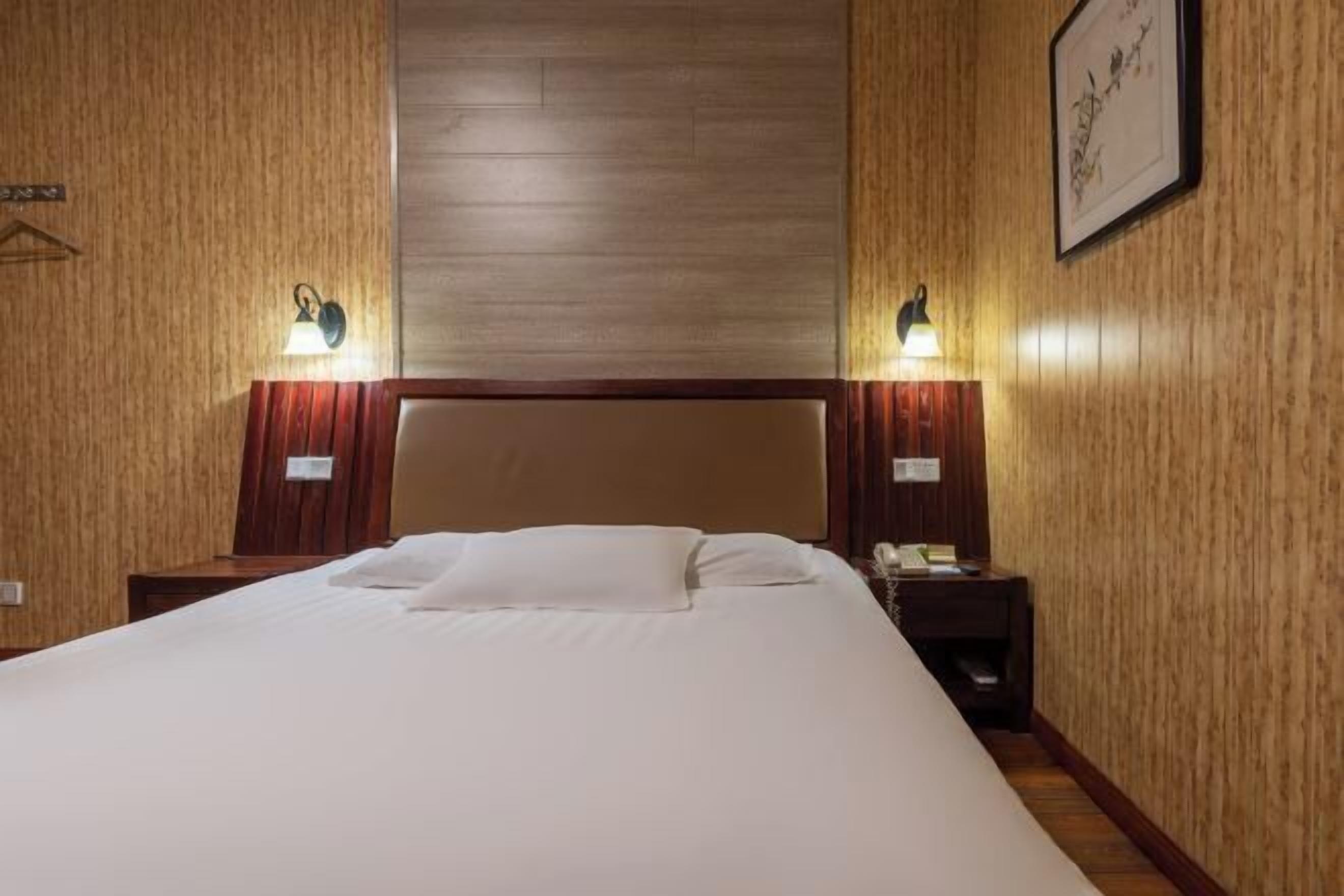 A hotel room with a large bed, wooden panel walls, and two bedside lamps.