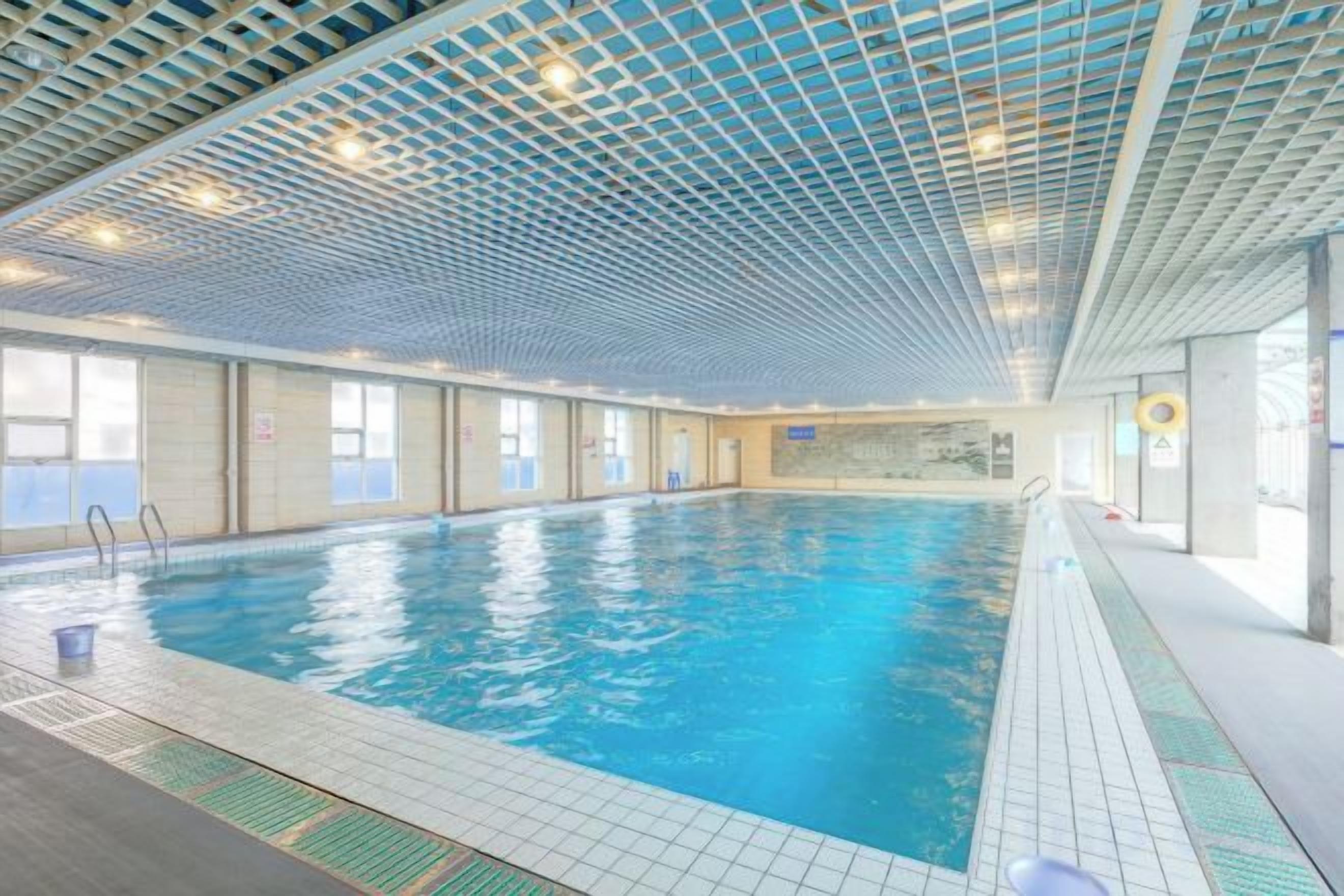 Une piscine intérieure avec un sol carrelé, un plafond transparent et des fenêtres sur un des côtés.
