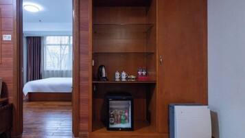 A hotel room with a wooden wardrobe, a bed, a small refrigerator, and a coffee maker.