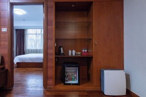 Ein Hotelzimmer mit Holzschrank, Bett, kleinem Kühlschrank und Kaffeemaschine.