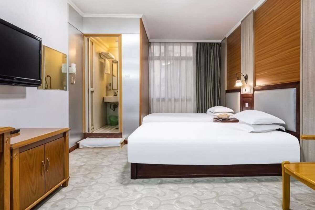 A hotel room with a bed, a TV, a desk, and a bathroom visible through an open door.
