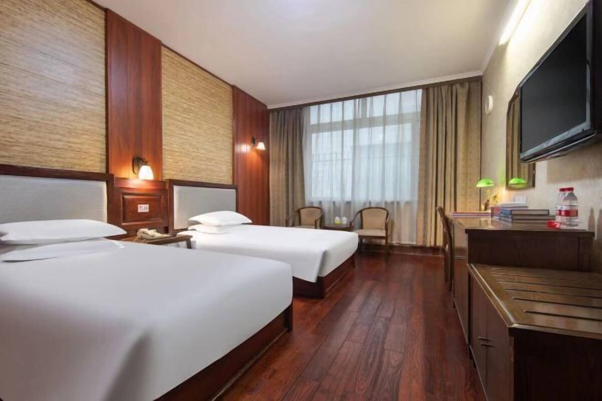 Habitación de hotel con dos camas, un escritorio, una silla, un televisor y una ventana con cortinas.