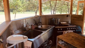 A rustic outdoor kitchen with a sink, stove, and storage shelves.