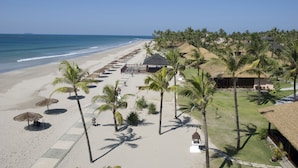 Ein Strandresort mit einer ausgedehnten Strandpromenade, Palmen und strohgedeckten Gebäuden.