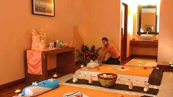 Une salle de spa équipée d’une table de massage, de bougies et d’un panier de fruits.