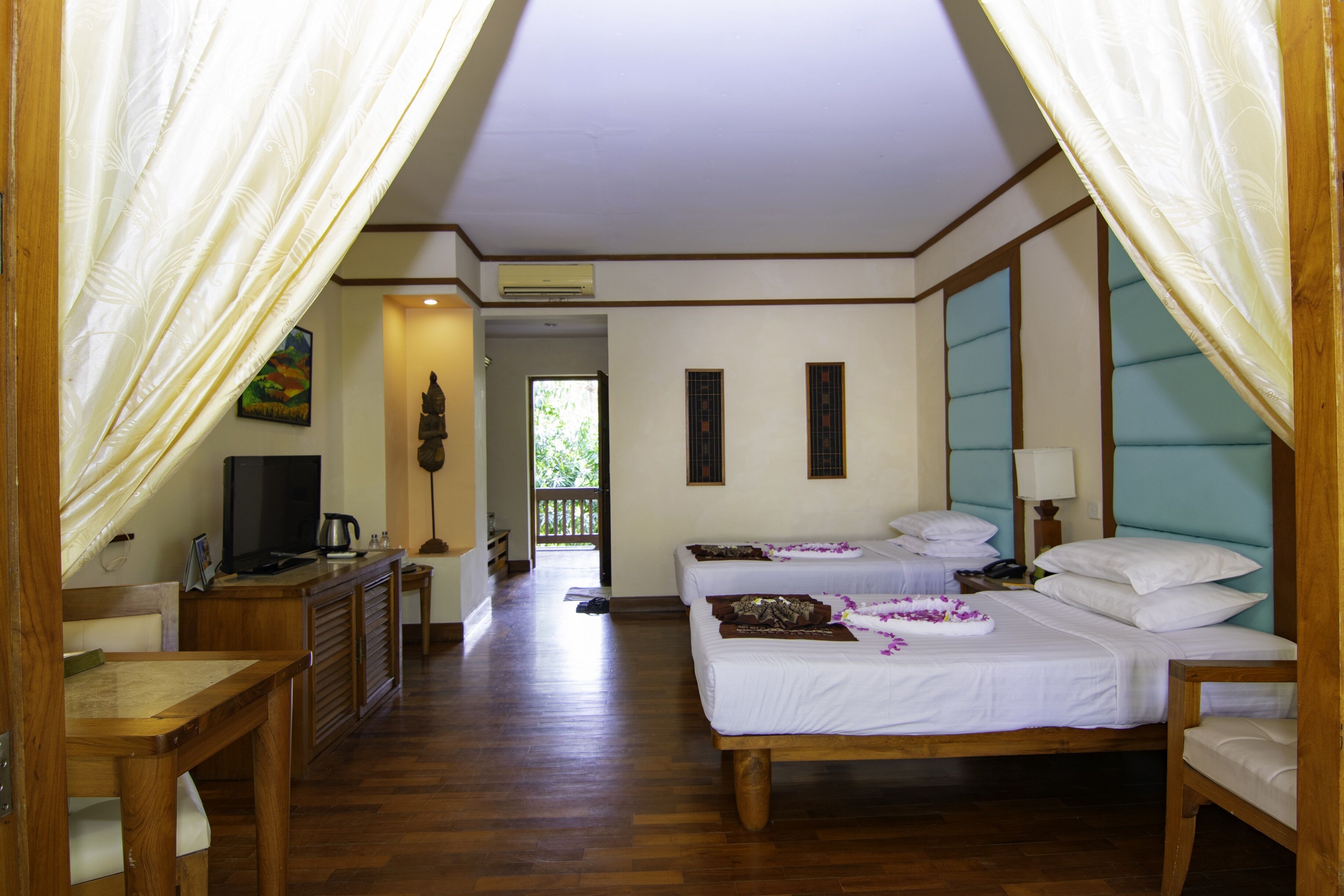 A hotel room with two beds, a TV, a desk, and a view of the outdoors.