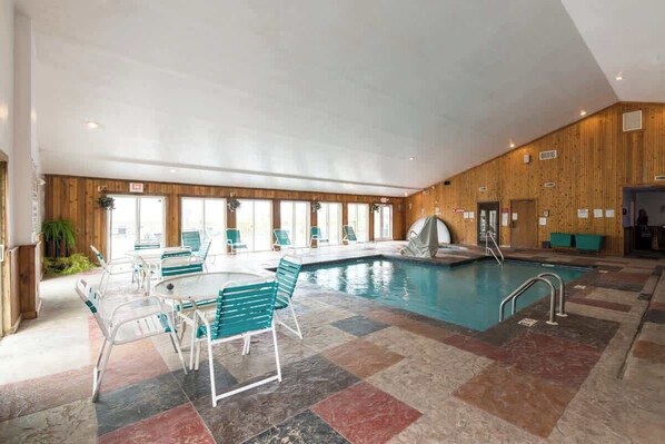 An indoor swimming pool with a tiled floor, lounge chairs, and a covered seating area.