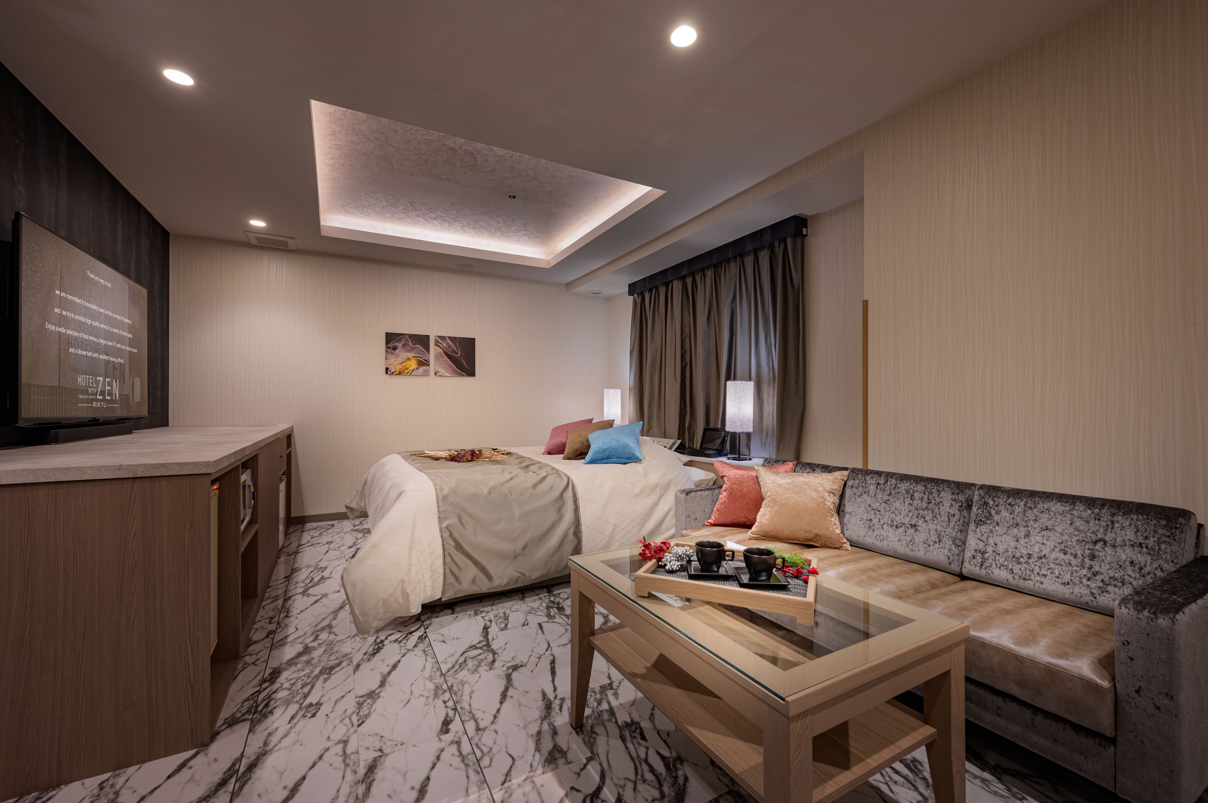 A hotel room with a bed, a sofa, a glass coffee table, a TV, and a desk.