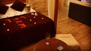 A bedroom with a stone wall, a bed with a dark red bedspread, a bedside table with a glass, and a small table with a glass and a box. - Character Suite ⭐️⭐️⭐️ (Milhaud)