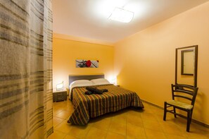 A hotel room with a bed, a chair, a nightstand, a lamp, and a painting on the wall. - Residence Hydria (Campofelice di Roccella)
