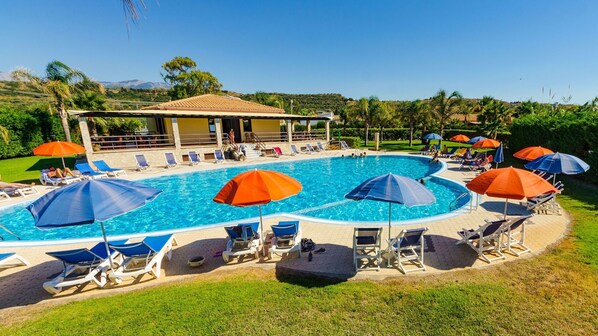 A swimming pool with lounge chairs and umbrellas, surrounded by a building with a tiled roof. - Residence Hydria (Campofelice di Roccella)