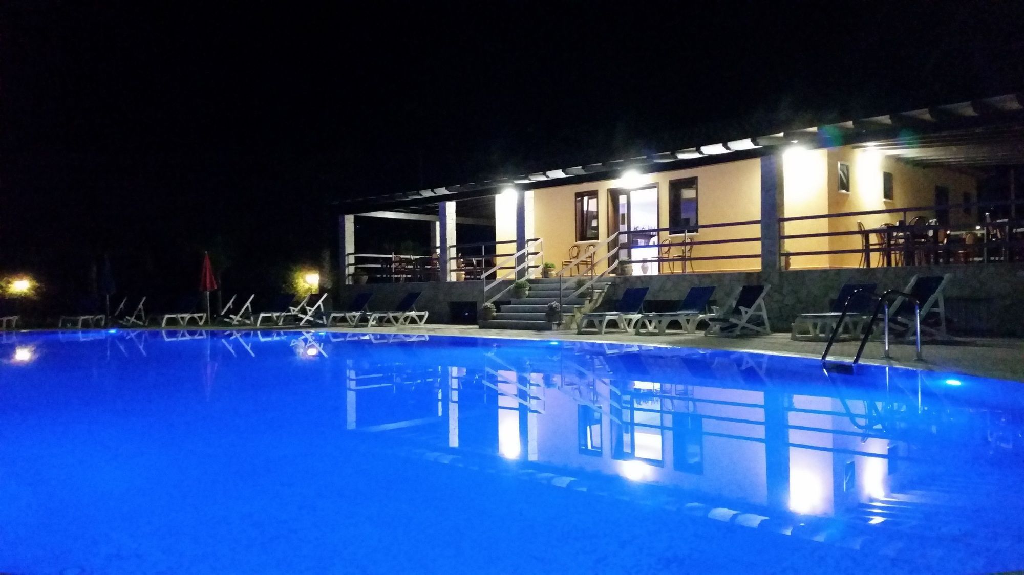 A nighttime swimming pool with lounge chairs and a building with steps leading to an entrance.