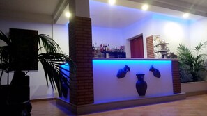 A reception area with a brick column, a blue-lit counter, and a display of various bottles. - Residence Hydria (Campofelice di Roccella)