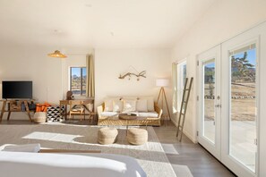A spacious room with a large bed, a sofa, a television, and a dining area. - Rancho Nopales JT-Pool, Hot Tub, Hammocks & Views (Joshua Tree)