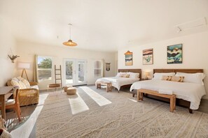 Ruime slaapkamer met een groot bed, twee kleinere bedden, een zithoek met een tafel en stoelen, en uitzicht op het omliggende landschap door een glazen deur.