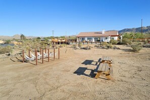 A desert landscape with a house, hammocks, and a picnic table. - Rancho Nopales JT-Pool, Hot Tub, Hammocks & Views (Joshua Tree)