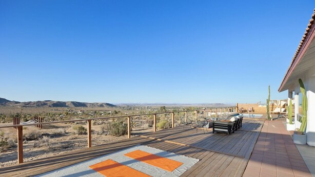 A wooden deck with a checkered rug, outdoor furniture, and a view of a desert landscape. - Rancho Nopales JT-Pool, Hot Tub, Hammocks & Views (Joshua Tree)