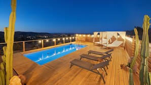 Ein Poolbereich auf dem Dach mit einer Holzterrasse, Liegestühlen und Kakteen.