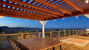 Eine Terrasse im Freien mit einem Holztisch und -stühlen, Blick auf die Landschaft und einer Pergola.