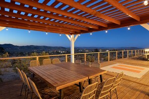 An outdoor deck with a wooden table and chairs, a view of the landscape, and a pergola structure. - Rancho Nopales JT-Pool, Hot Tub, Hammocks & Views (Joshua Tree)