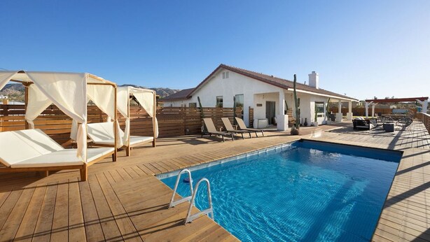 Ein Poolbereich mit Holzterrasse, einem klaren blauen Pool und Liegestühlen.