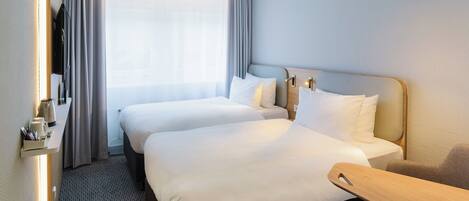 Habitación de hotel con dos camas, un escritorio, una silla, cafetera y ventana con cortinas.