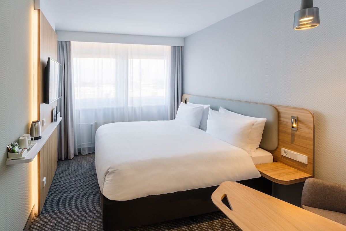 Une chambre d’hôtel avec un grand lit, des tables de chevet, une télévision et une fenêtre avec des rideaux.