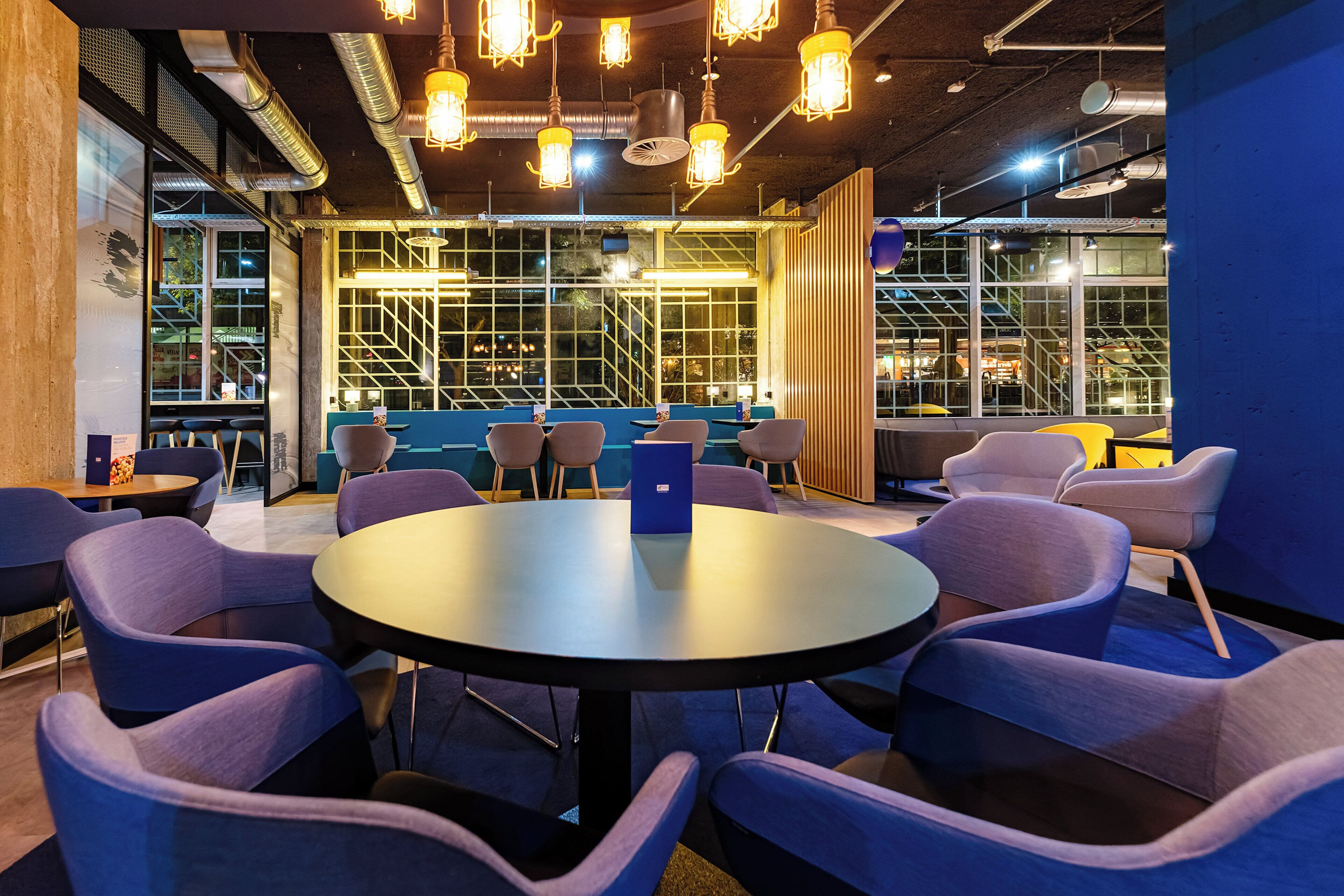 A modern meeting room with round tables and chairs, large windows, and industrial-style lighting.