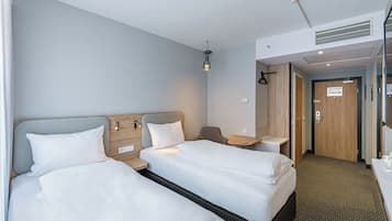 Ein Hotelzimmer mit zwei Betten, einem Schreibtisch, einem Spiegel und einer Tür zu einem Badezimmer.