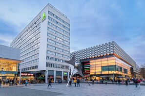 Un edificio moderno con una llamativa estructura en forma de estrella, rodeado de tiendas y un hotel.