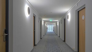 Un pasillo de hotel con puertas a ambos lados, una alfombra estampada y una señal de salida verde.