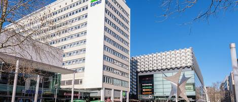 A modern hotel with a prominent green logo, a glass facade, and a distinctive star-shaped sculpture in front.