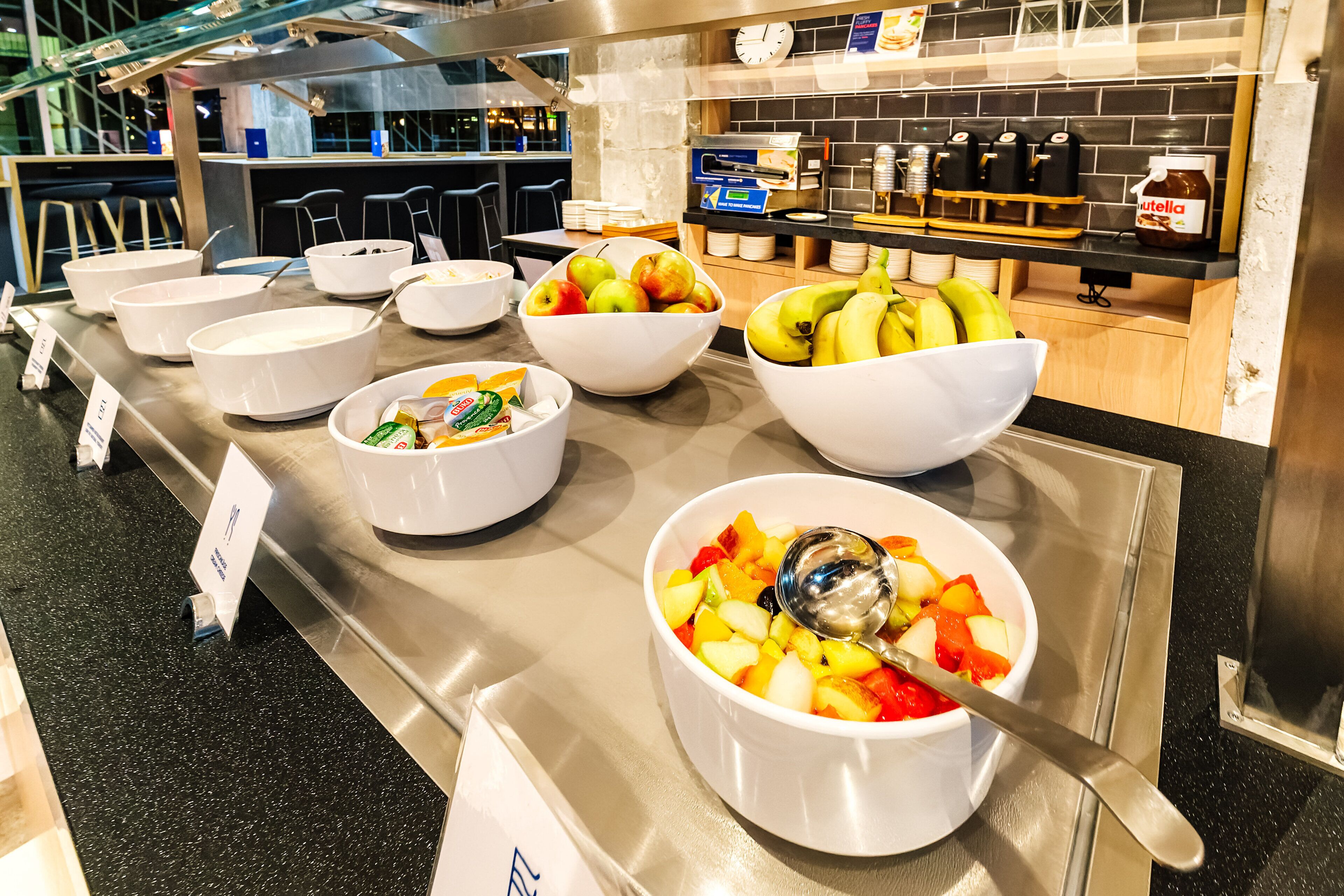 A buffet with various bowls of fruits and a coffee station.