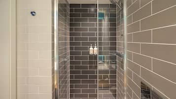 Un baño moderno con ducha envuelta en vidrio, paredes de azulejos oscuros y un lavabo blanco.