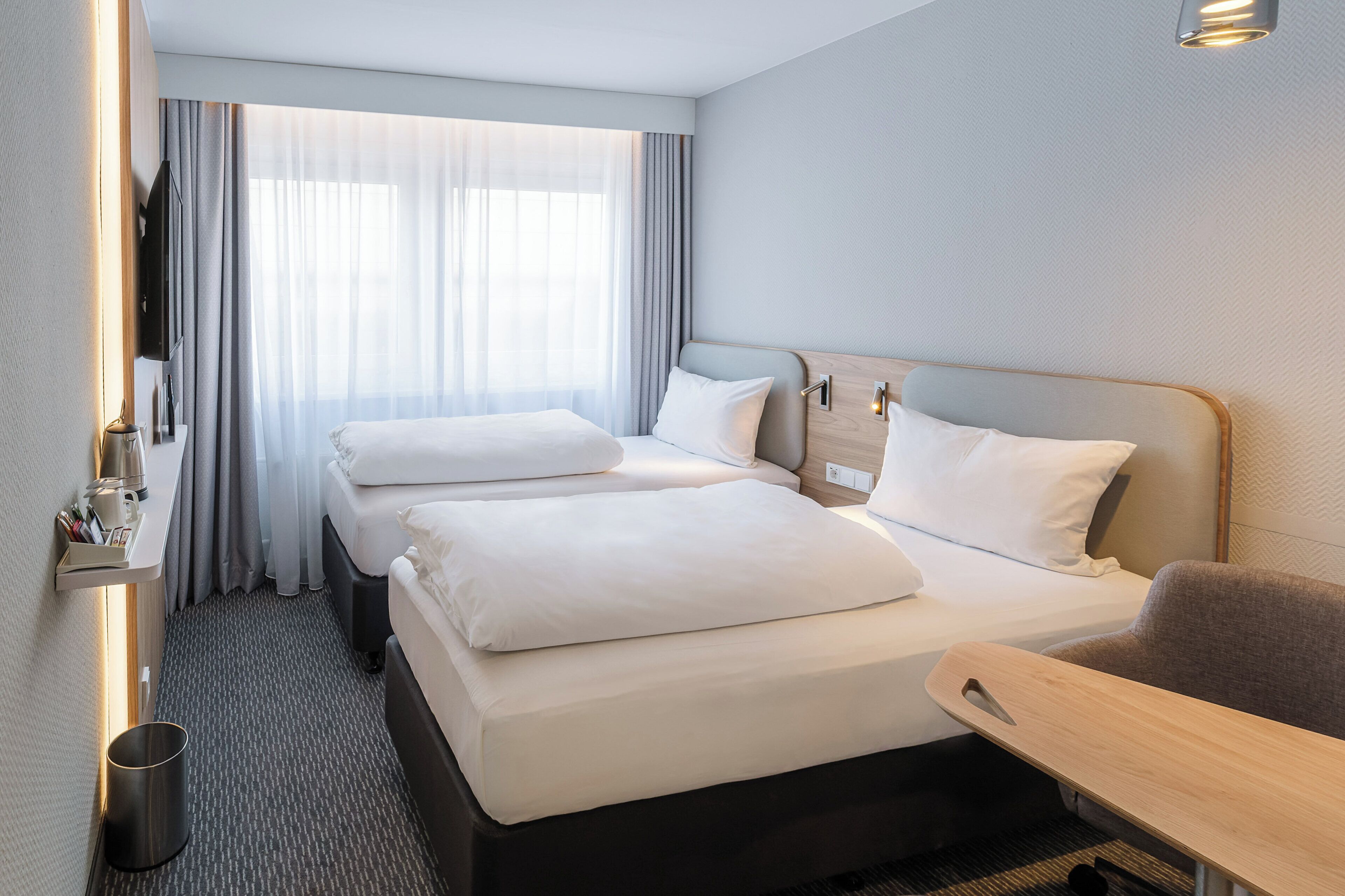 Quarto de hotel com duas camas, uma escrivaninha, uma cadeira, uma televisão e uma janela com cortinas.