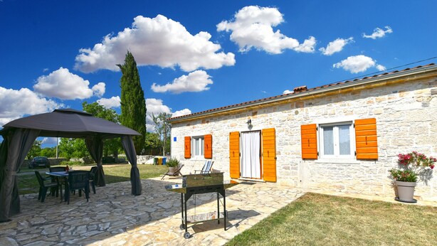 A stone building with orange shutters, a covered patio with chairs, and a lawn. - House 2176/55604 (Istria - Debeljuhi), 19000m from the beach (Debeljuhi)