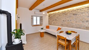 A cozy room with a stone wall, wooden beams, a white sofa, a table with chairs, and a black stove. - House 2176/55604 (Istria - Debeljuhi), 19000m from the beach (Debeljuhi)