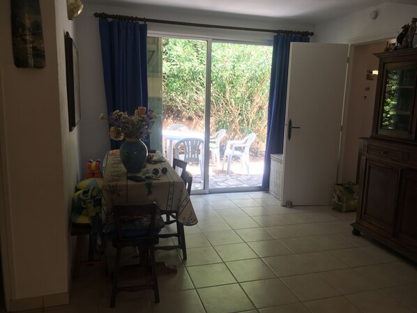Un comedor con una mesa, sillas, un florero con flores y vistas a un patio exterior con sillas a través de una puerta de cristal.