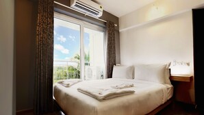 Una habitación de hotel con una cama grande, un equipo de aire acondicionado, una ventana con cortinas y una mesita de noche.