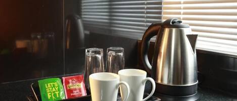 A kitchen counter with a tea tray, two white mugs, a stainless steel kettle, and two glass bottles.