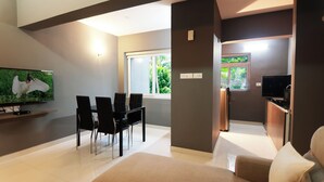 Una sala moderna con un televisor de pantalla plana, un comedor con sillas, un sofá y una zona de cocina con un refrigerador.