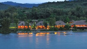 A riverside hotel with multiple buildings, each featuring a thatched roof and illuminated windows. - One Myanmar Resort Putao (Putao)