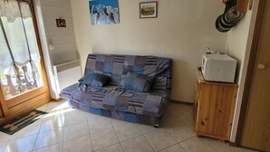 A living room with a sofa, a door, a radiator, and a small cabinet with kitchen items.