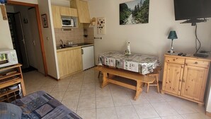 A compact living space with a kitchenette, a dining table, a TV, and a bed.