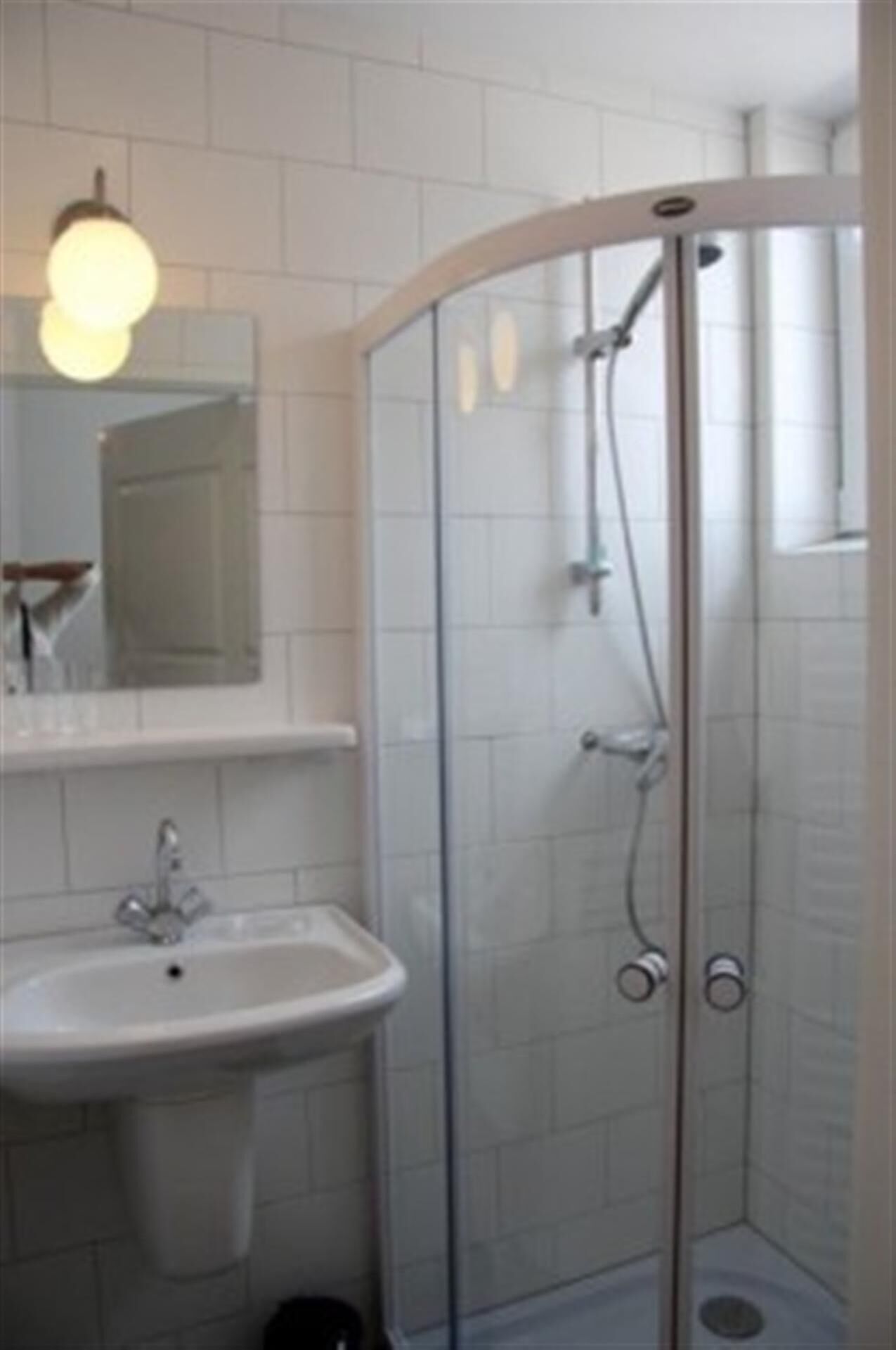 Un baño con cabina de ducha de vidrio, un lavabo blanco y un espejo sobre el lavabo.